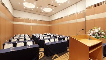 Una sala conferenze con file di tavoli, sedie e un podio con un microfono.