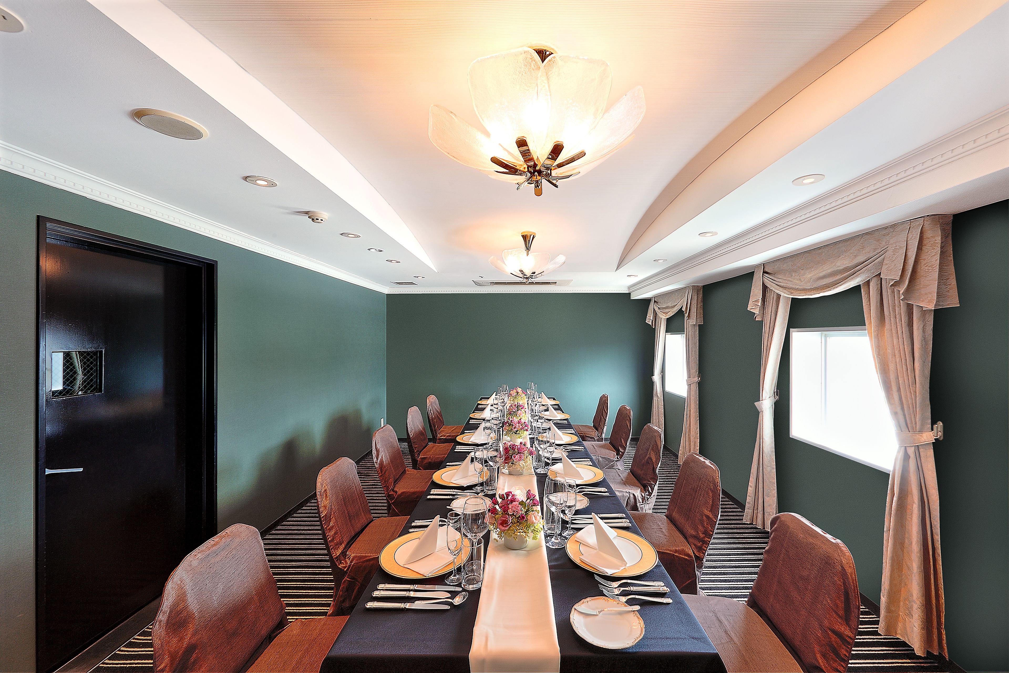 A conference room with a long table set for a meeting, equipped with chairs, a projector screen, and a ceiling light fixture.