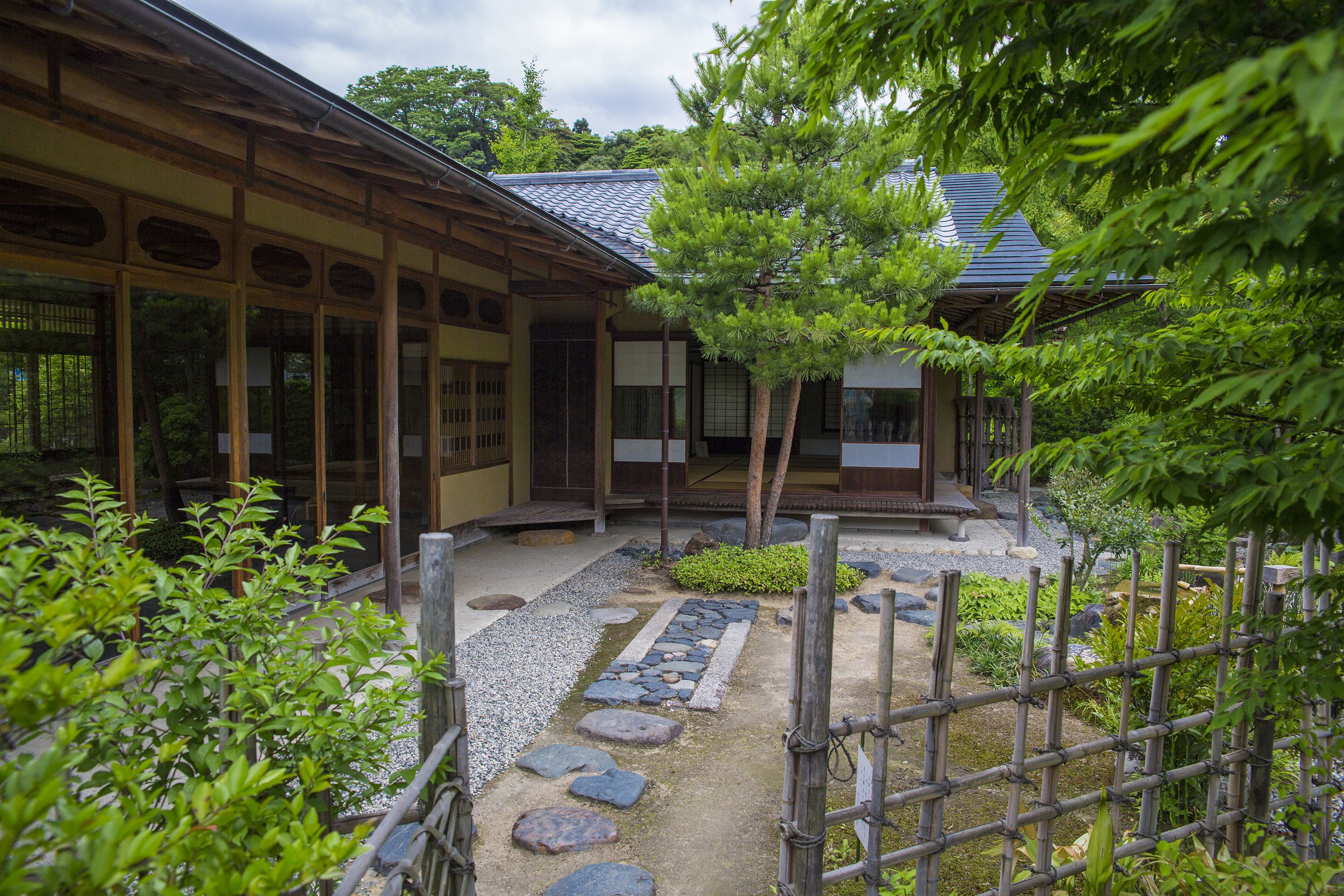 A traditional Japanese building with a wooden exterior, a stone pathway, and a bamboo fence.