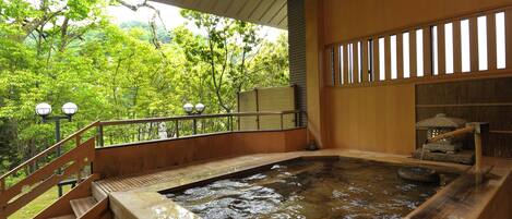 Zona de baño termal con barandillas de madera, un farol de piedra y vistas a vegetación exuberante.