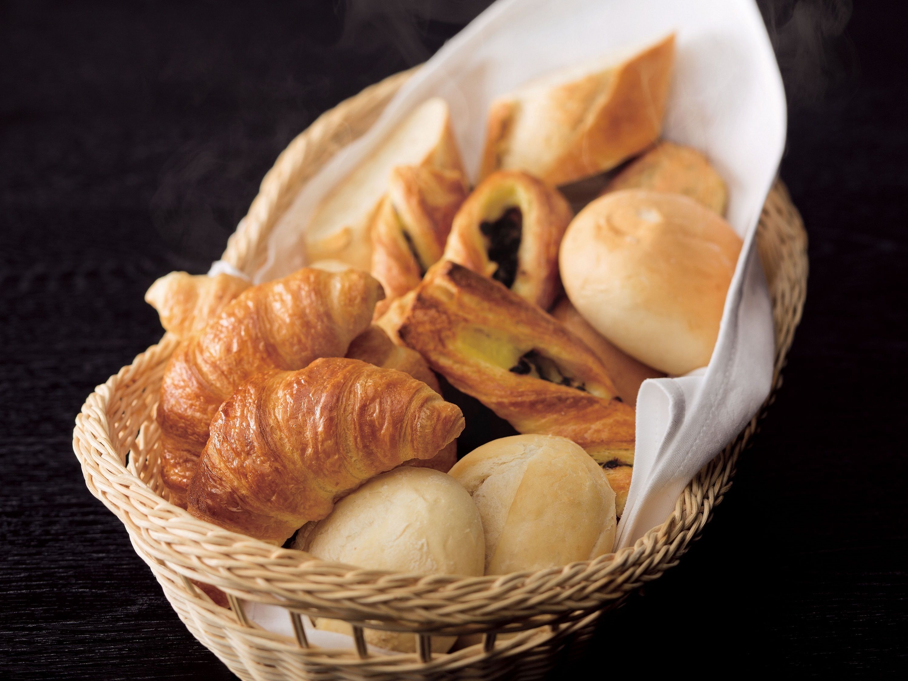A basket containing various types of bread, including croissants and rolls.