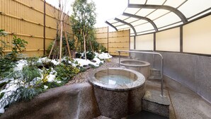 Un onsen japonais traditionnel, avec des bains à remous en pierre, une clôture en bois et une bambouseraie.