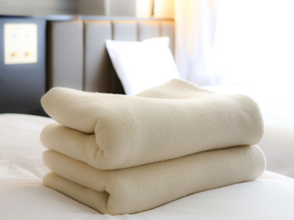 A neatly folded beige blanket on a bed with a white pillow and a headboard in the background.