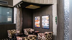 Un espace détente avec des chaises et des tables ornées de motifs floraux, un tapis à rayures noires et blanches, et deux affiches accrochées au mur.