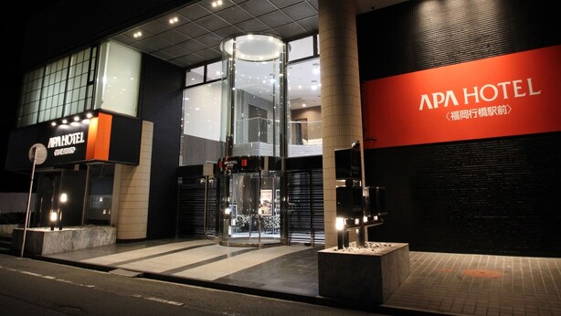 L’extérieur de l’hôtel APA présente un design moderne, avec une entrée imposante dotée de portes vitrées et d’un luminaire vertical.