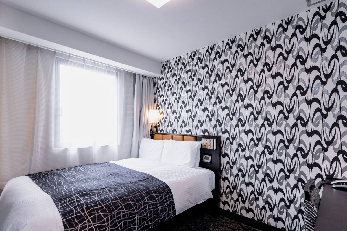 Ein Hotelzimmer mit Bett, Nachttisch, Lampe und Wandpapier mit Muster.
