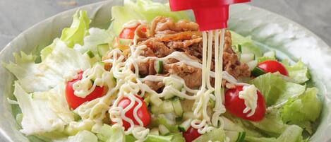 A salad with lettuce, tomatoes, cucumbers, and noodles being dressed with a white sauce.