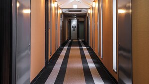 A hotel hallway with a striped carpet, wooden walls, and wall-mounted lights. - APA Hotel Saga Ekimae Chuo (Saga)