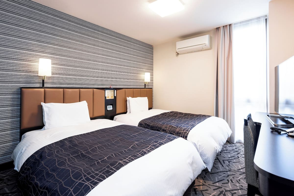 Ein Hotelzimmer mit zwei Betten, einem Schreibtisch und einem großen Fenster.