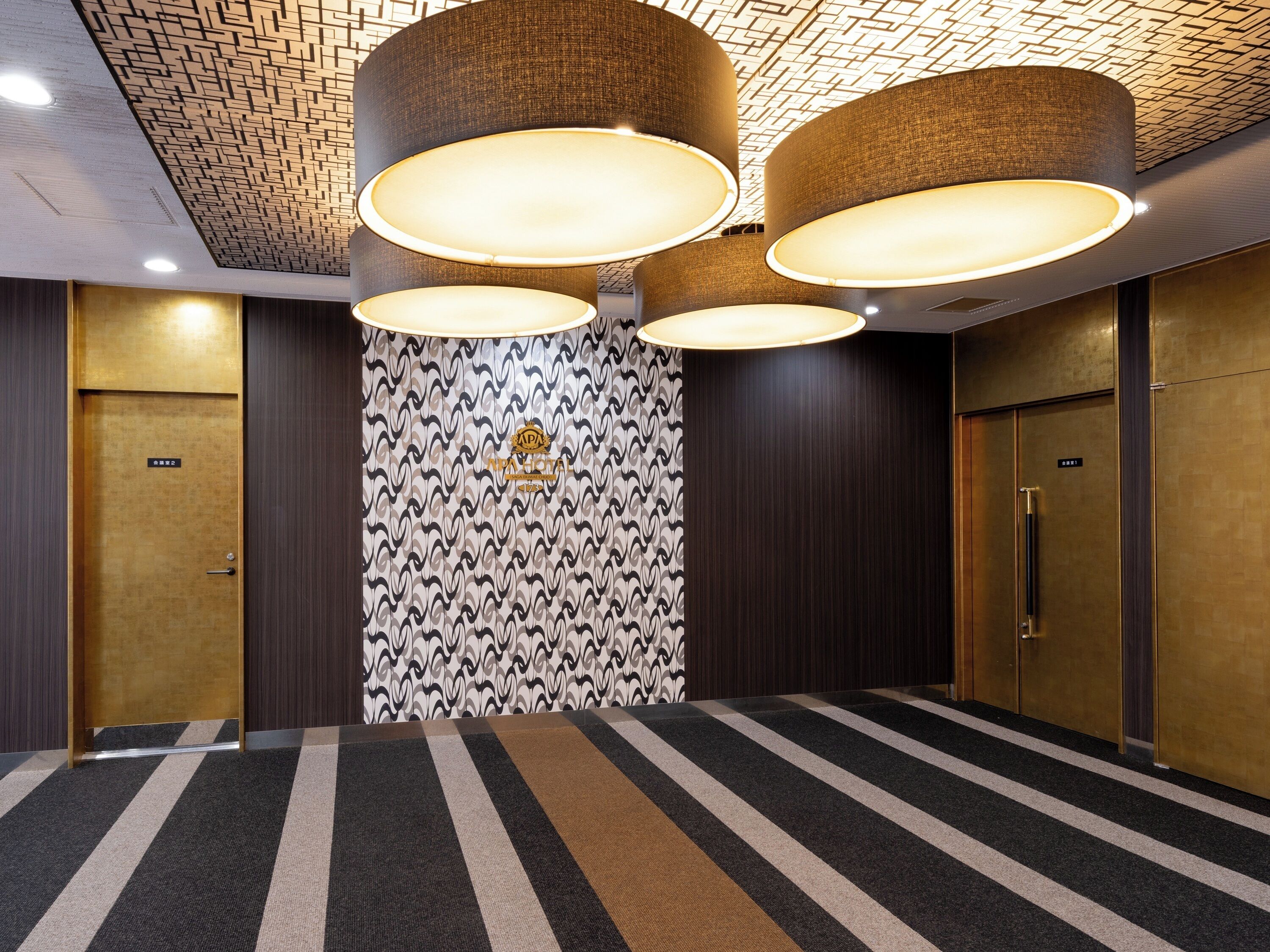 A conference room with a striped carpet, two large cylindrical lamps, and a patterned wall with a logo.