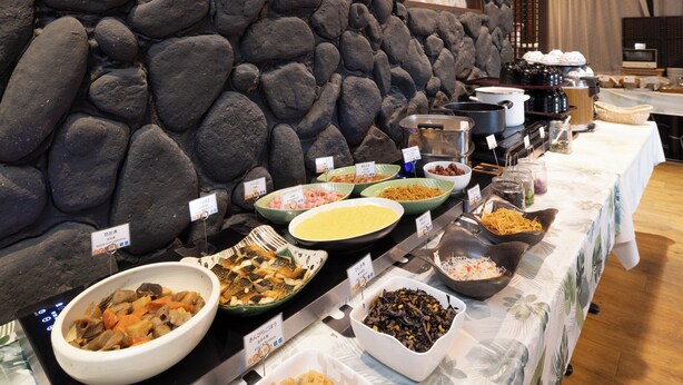 A buffet table with various dishes, including seafood, vegetables, and other prepared foods, set against a stone wall backdrop. - APA Hotel Saga Ekimae Chuo (Saga)