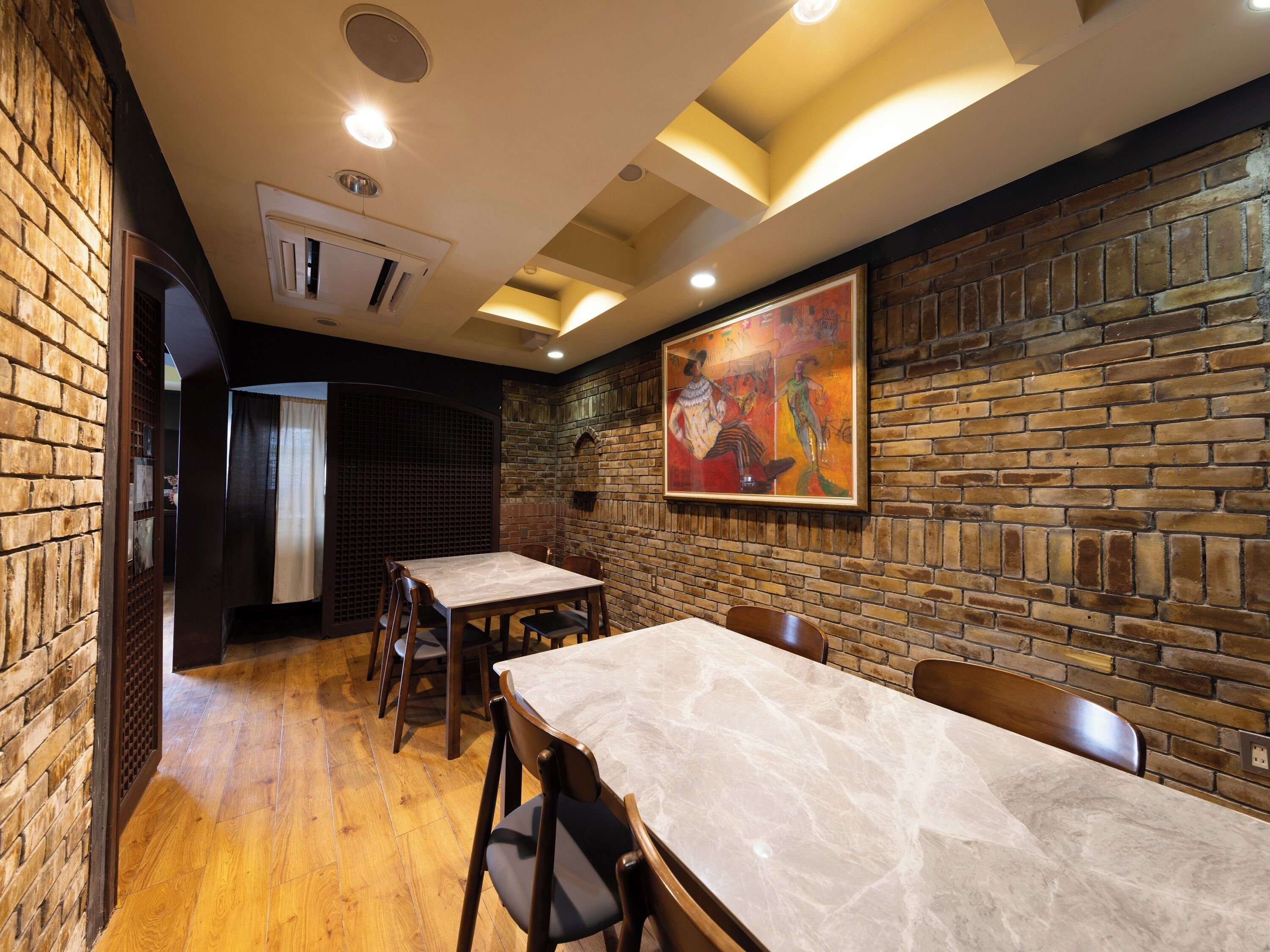 Interior de restaurante con paredes de ladrillo, piso de madera y un mural grande. Mesas y sillas dispuestas para comer.
