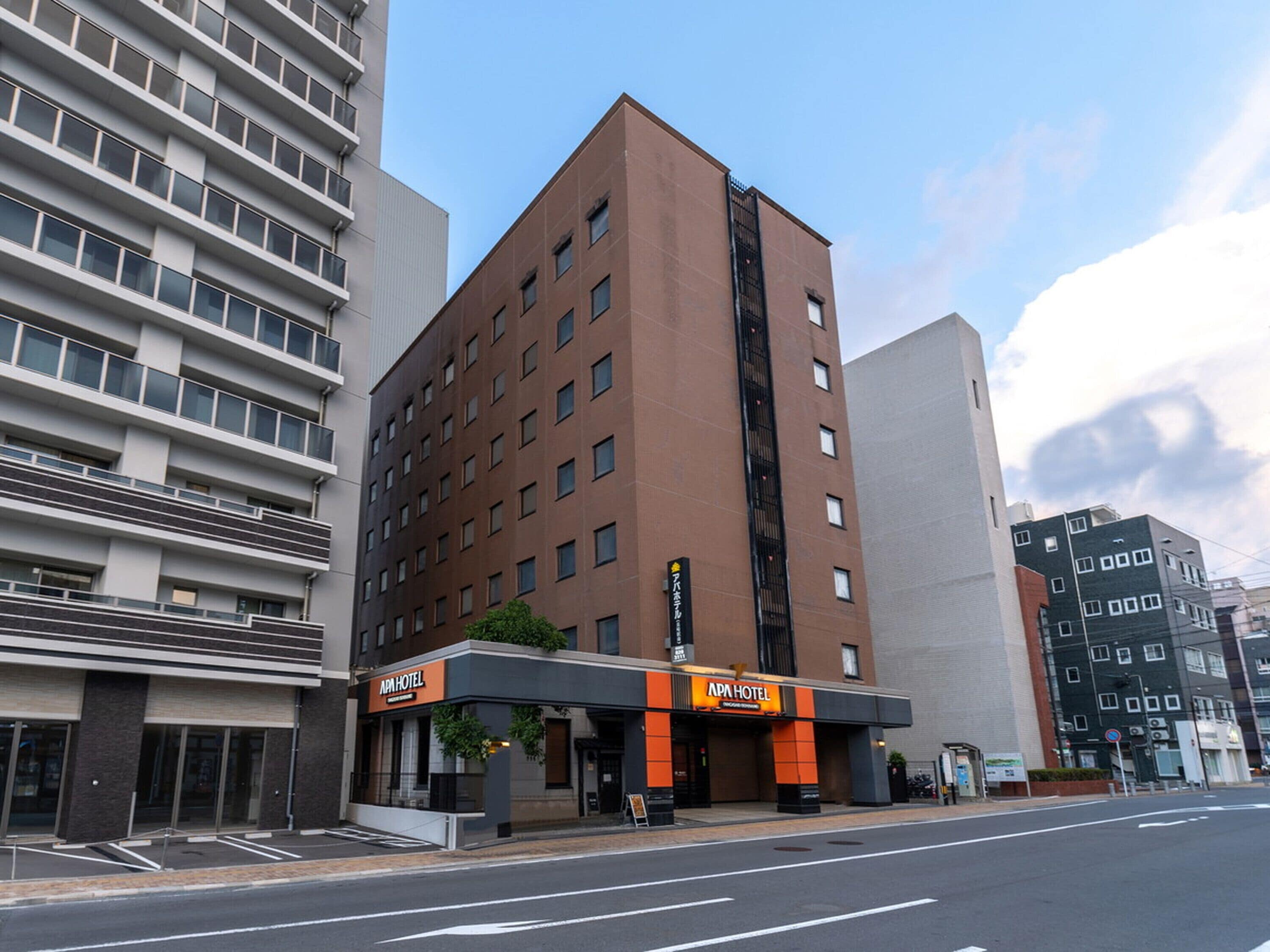 Een modern hotel met een bruine gevel, meerdere verdiepingen en een opvallend 'APA HOTEL' bord.