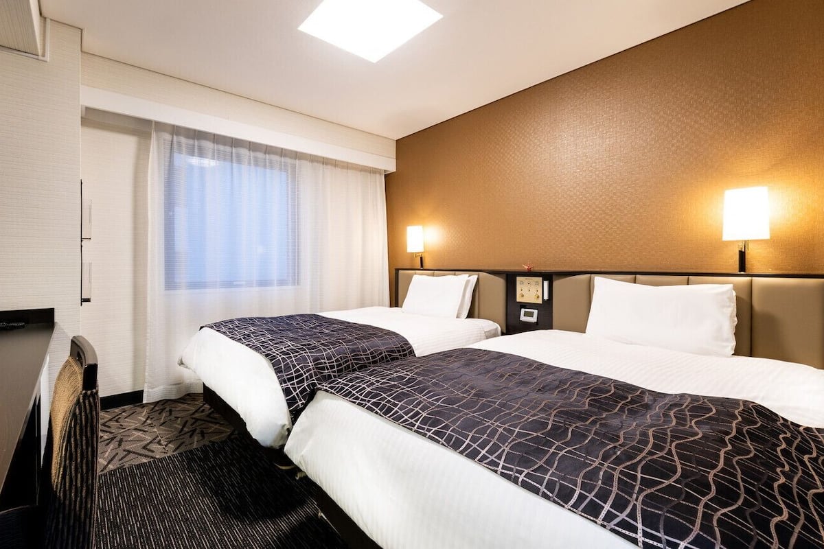Une chambre d’hôtel avec deux lits, un bureau, une télévision et une fenêtre avec des rideaux.