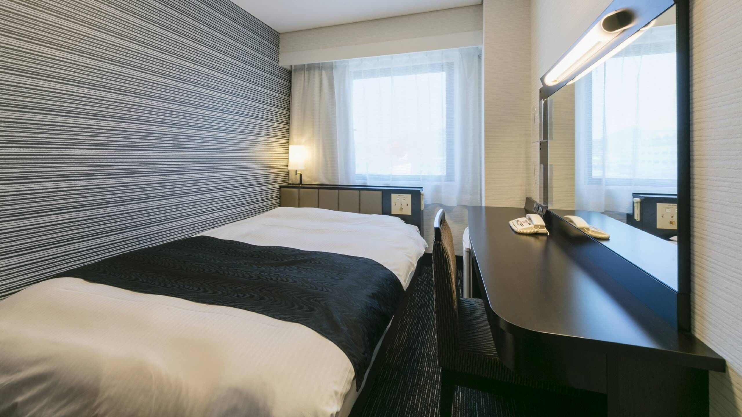 A hotel room with a bed, a desk, a mirror, and a window.