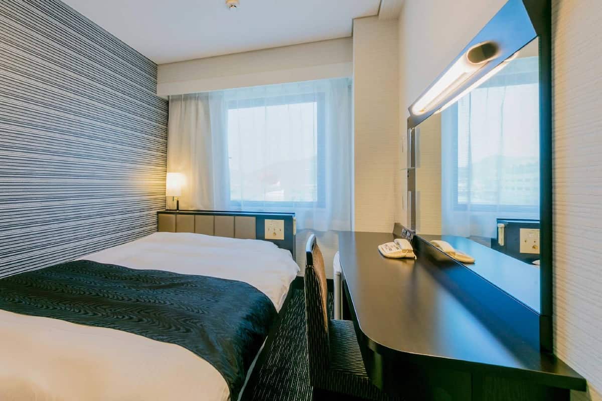 A hotel room with a bed, bedside table, lamp, and a large mirror.