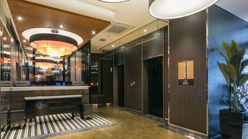 A modern lobby with a reception desk, a staircase, and a large potted plant.