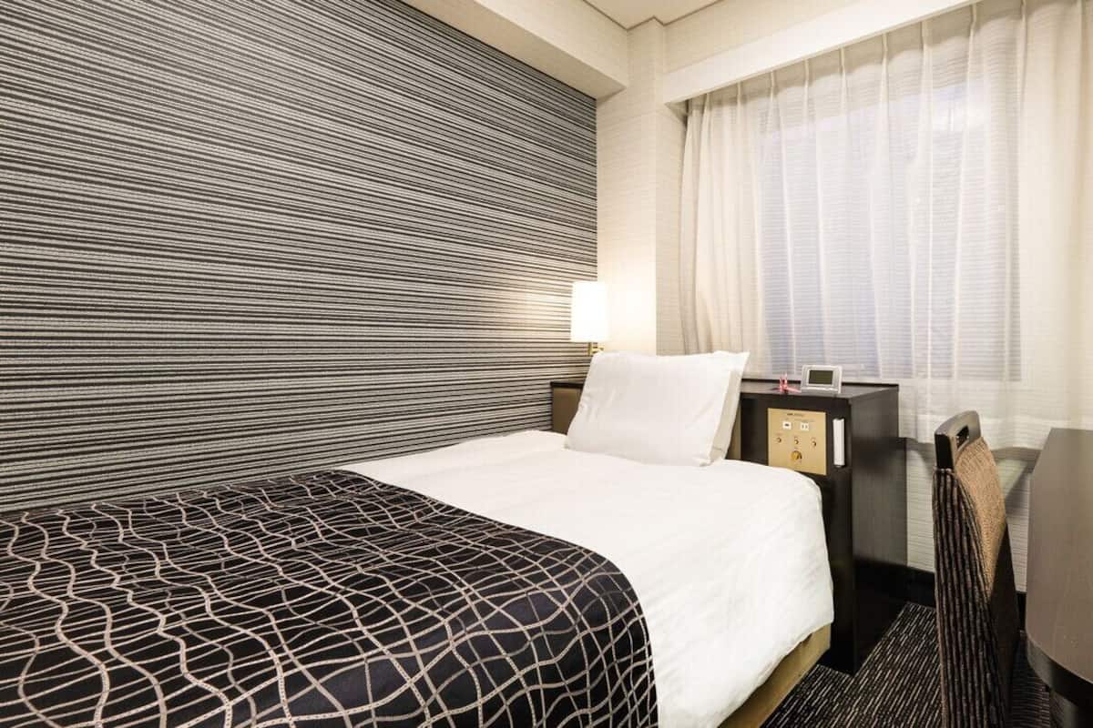 Une chambre d’hôtel avec un lit, un bureau, une chaise, une table de chevet et une fenêtre avec des rideaux.