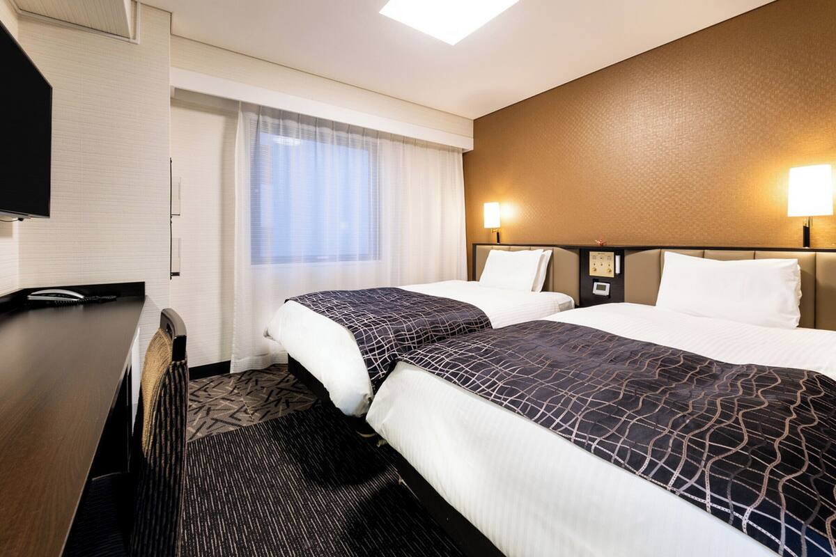 A hotel room with two beds, a desk, and a TV.