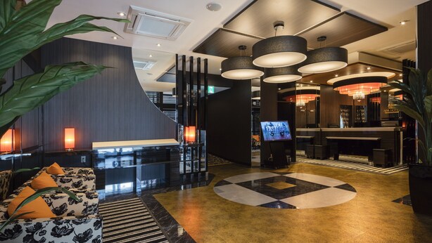 Un hall d’hôtel moderne avec un comptoir d’accueil, un espace salon et un grand lustre.