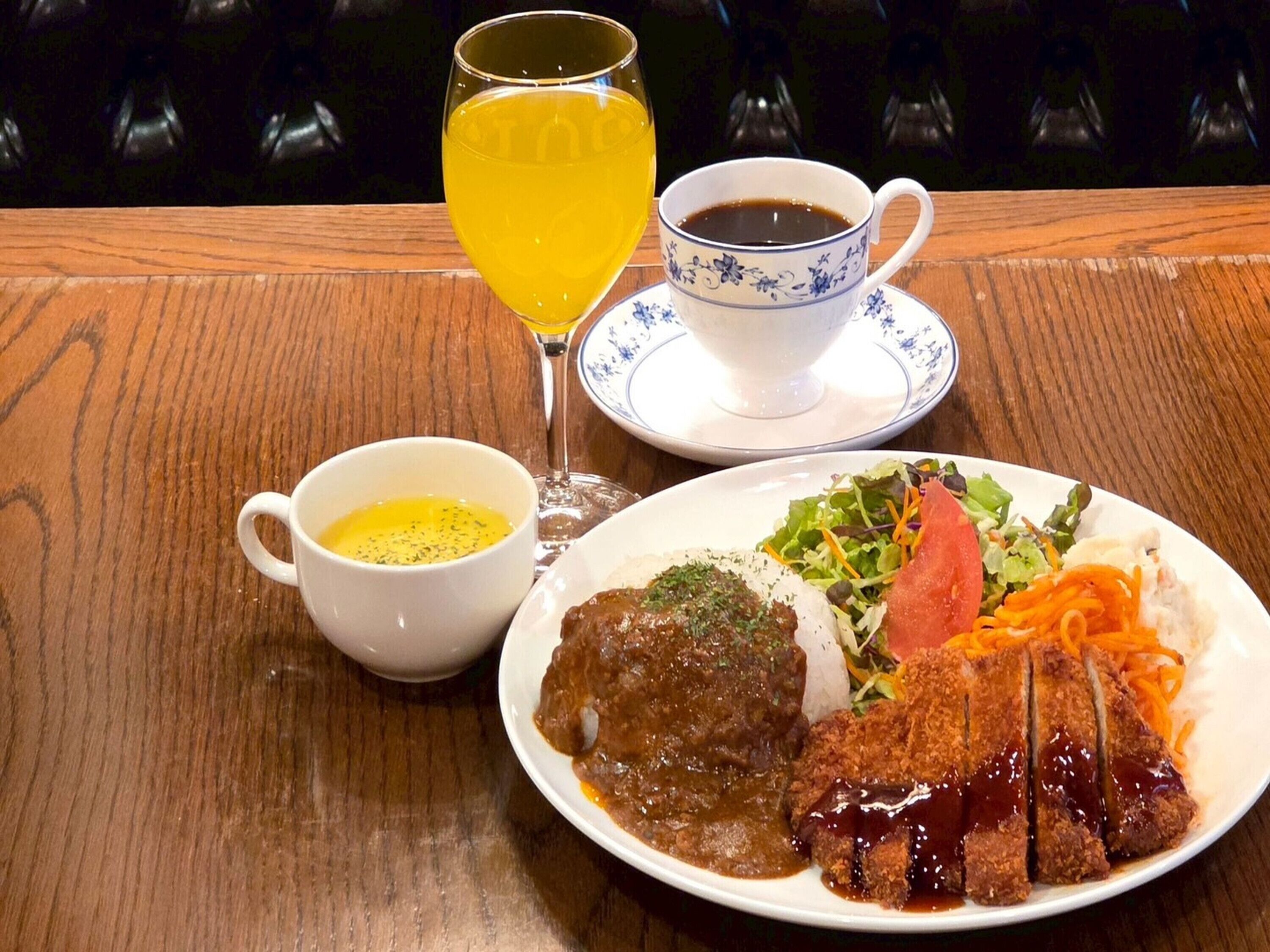 A dining table with a plate of food, a cup of coffee, a glass of juice, and a small bowl of sauce.