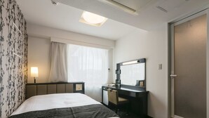 A hotel room with a bed, a desk, a mirror, and a window with curtains.