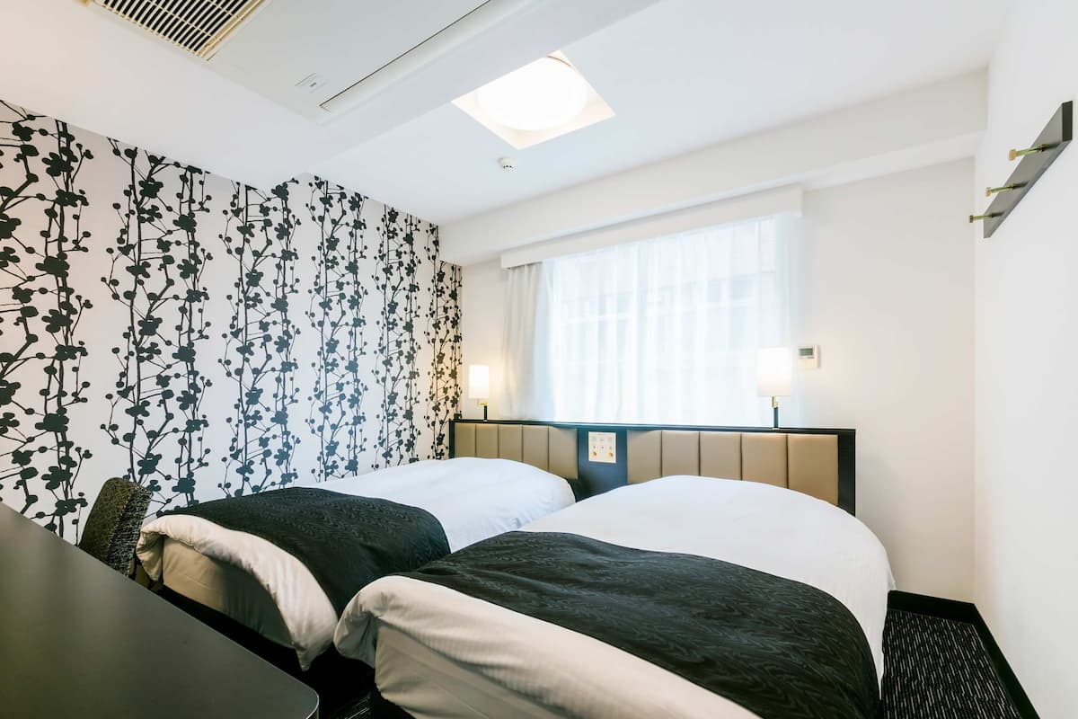 A hotel room with two beds, a desk, and a window with curtains.
