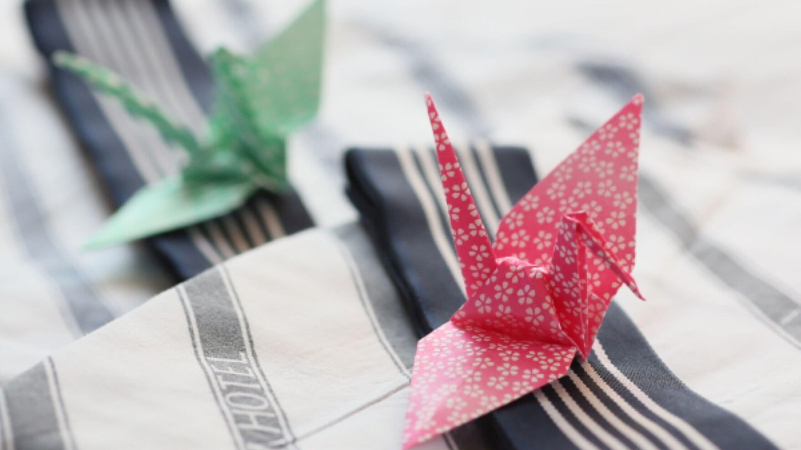 Zwei Papierorigami-Vögel auf einer gestreiften Fläche, mit einem Hotelschild.