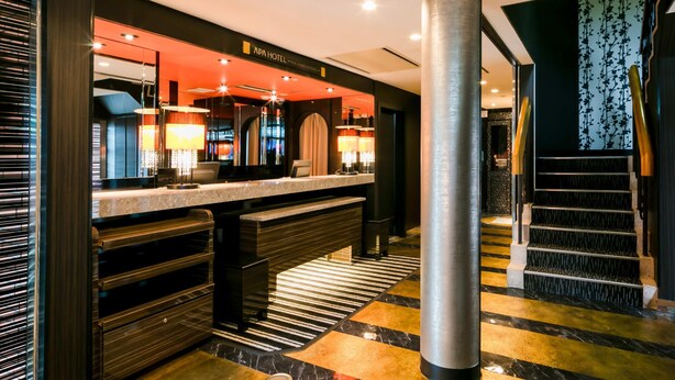 A modern hotel lobby with a reception desk, a large pillar, and a staircase.