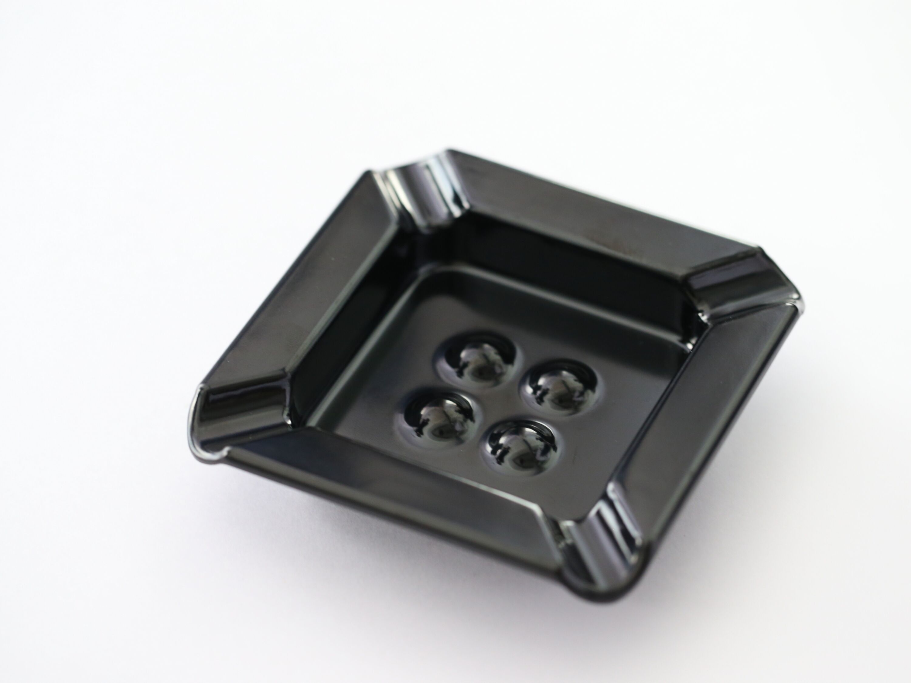A black, square-shaped object with four circular indentations, likely a metal component or part.
