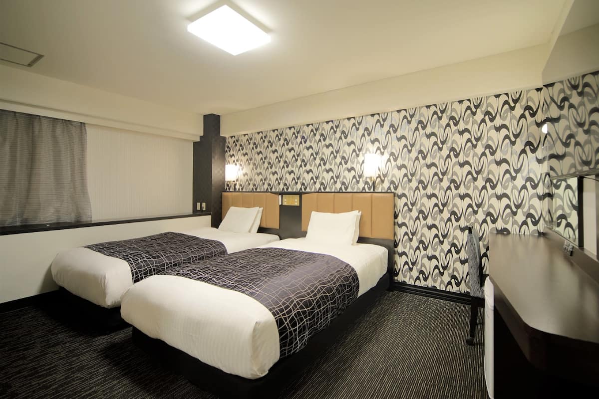 A hotel room with two beds, a desk, and a patterned wallpaper.