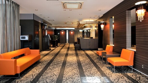 Eine Hotelhalle mit einem gemusterten Teppich, orangenen Sitzmöglichkeiten, einem Empfangstresen und einem modernen Deckenbau.