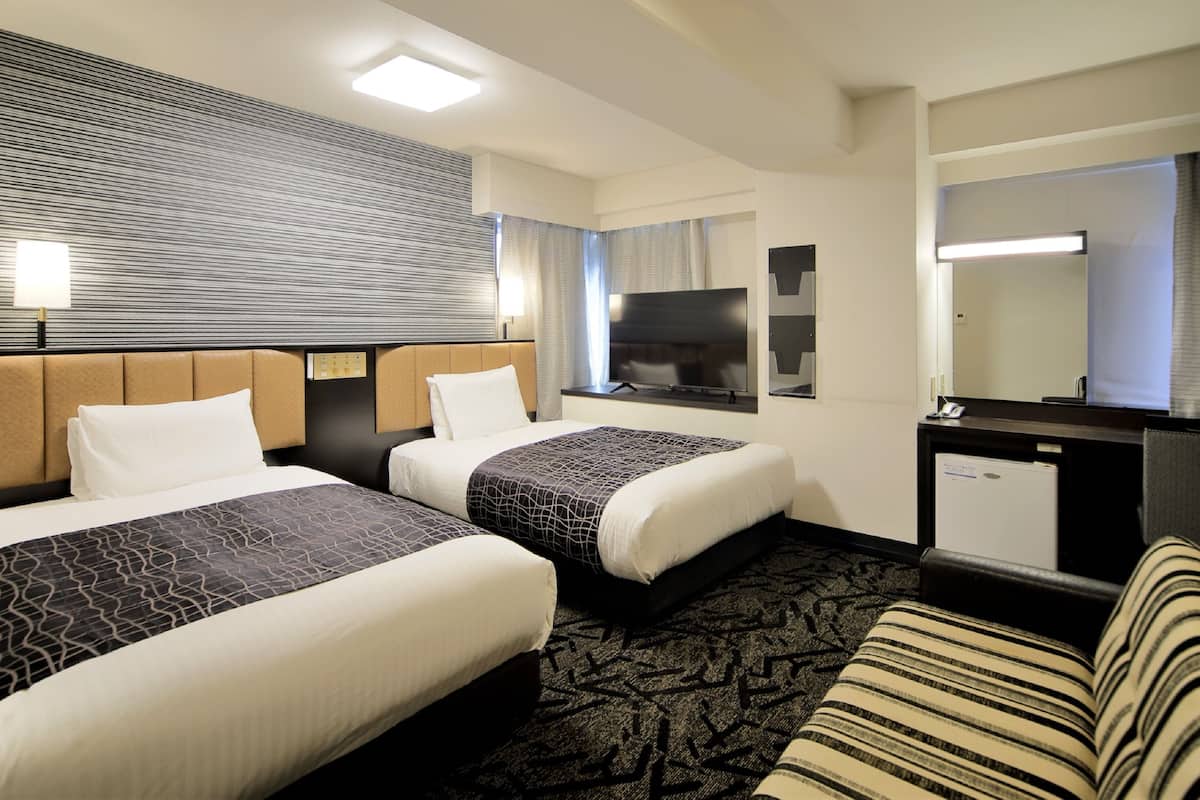 A hotel room with two beds, a TV, a desk, and a large mirror.