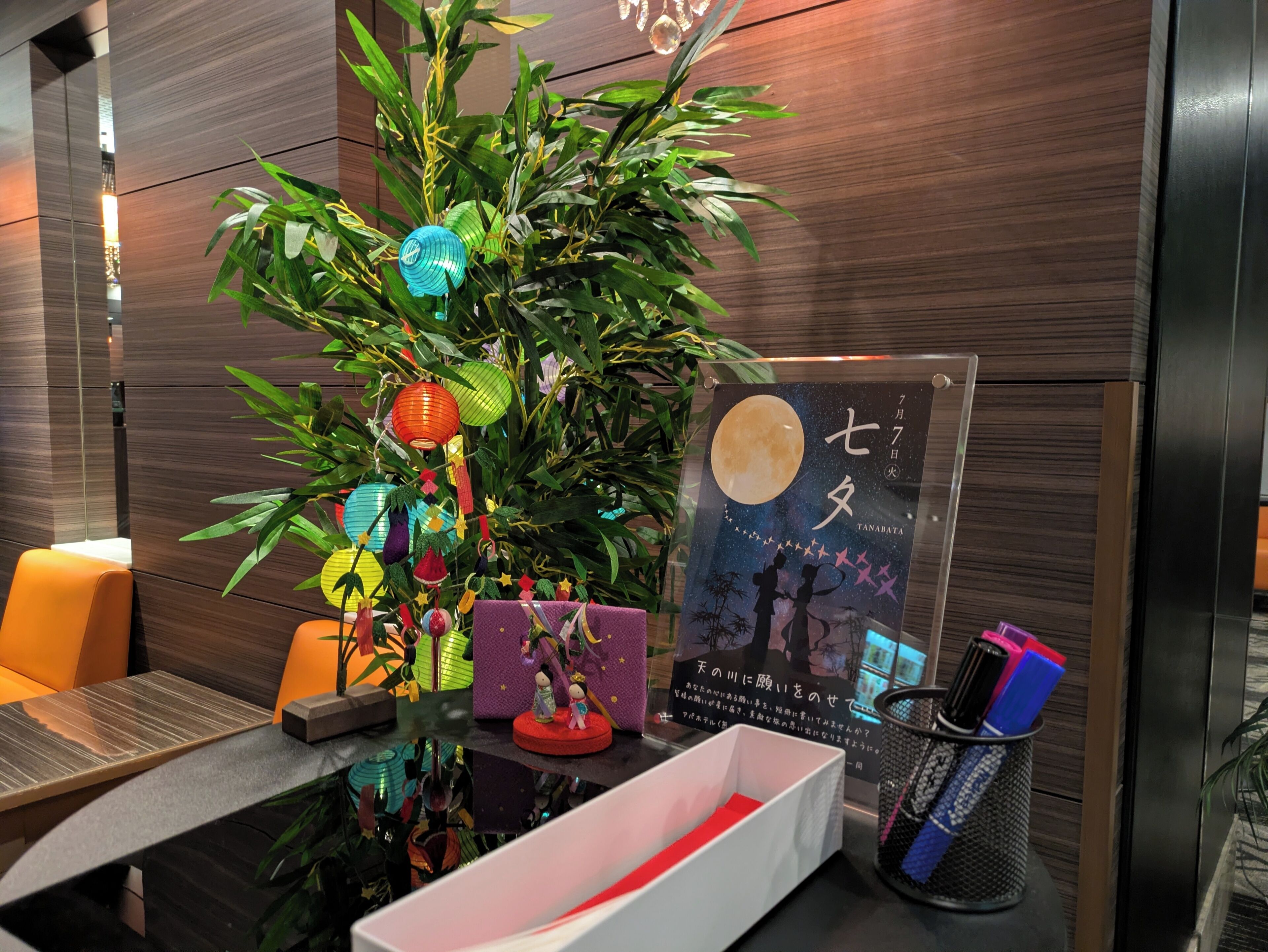 Een moderne hotelkamer met een houten wand, een decoratieve plant, een ingelijste poster en een tafel met een pennenhouder.