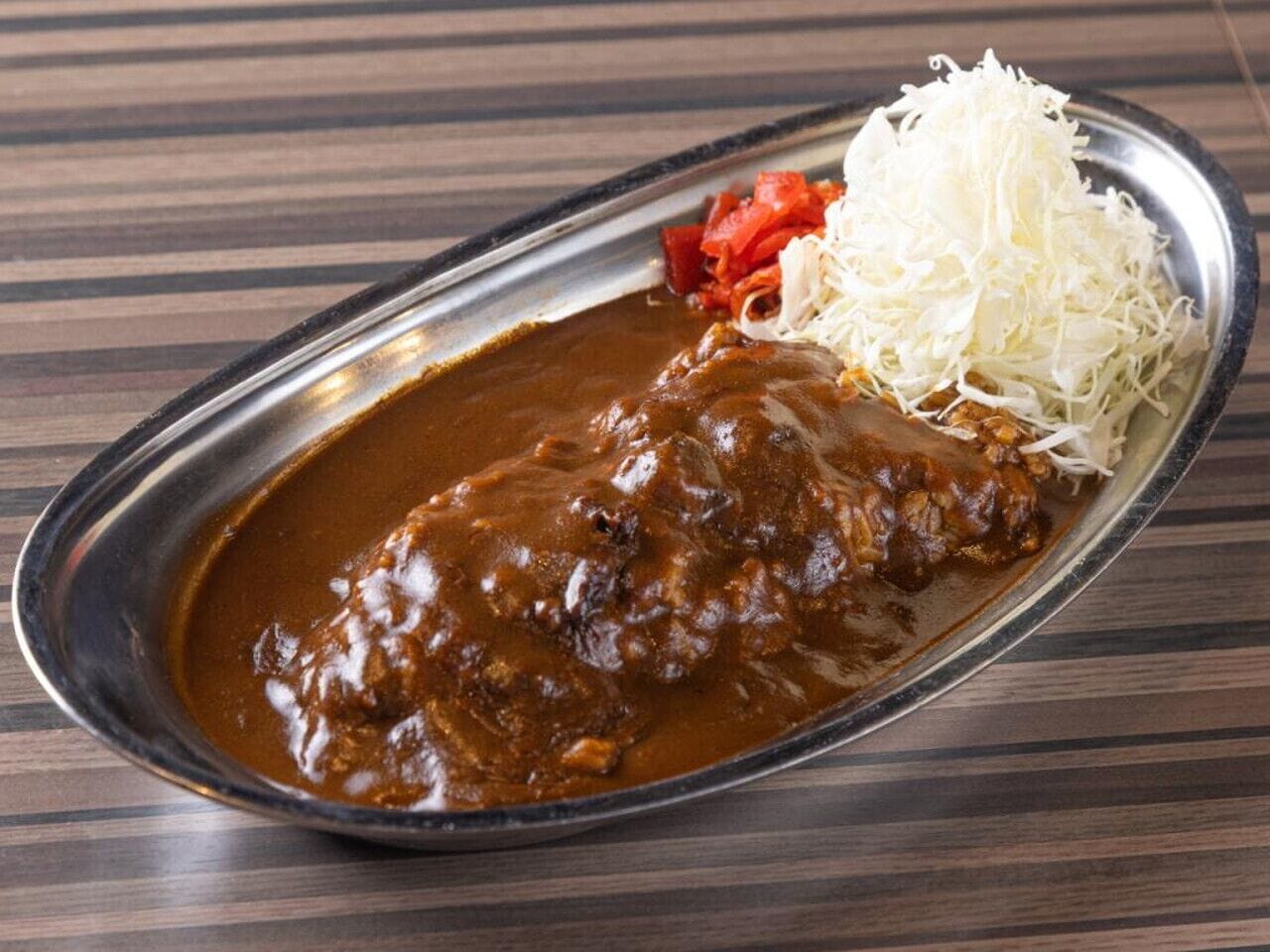 A plate with a meat dish, shredded white vegetable, and red pepper.