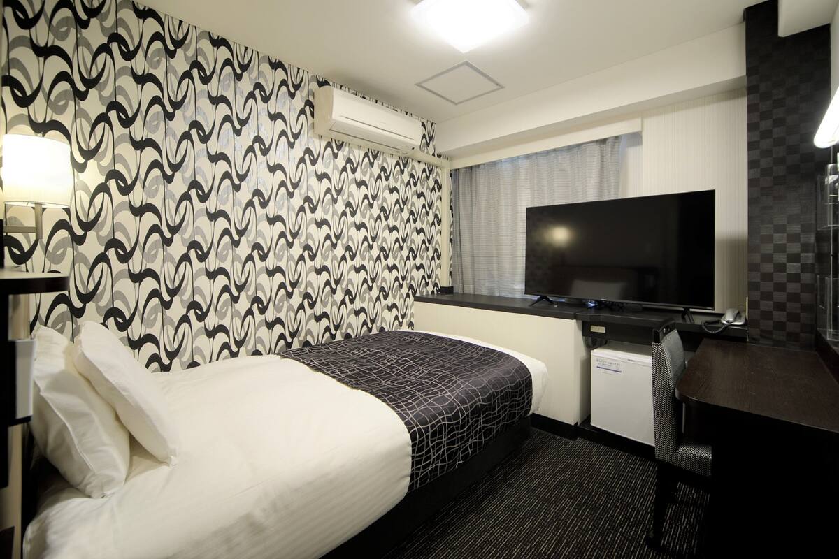 A hotel room with a bed, a desk, a television, and an air conditioning unit.