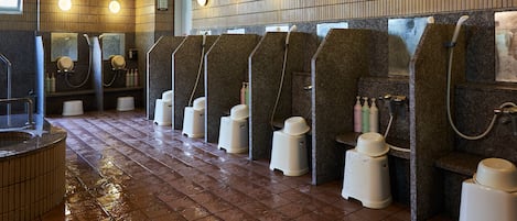 A public restroom with multiple urinals, a hand dryer, and a trash bin.