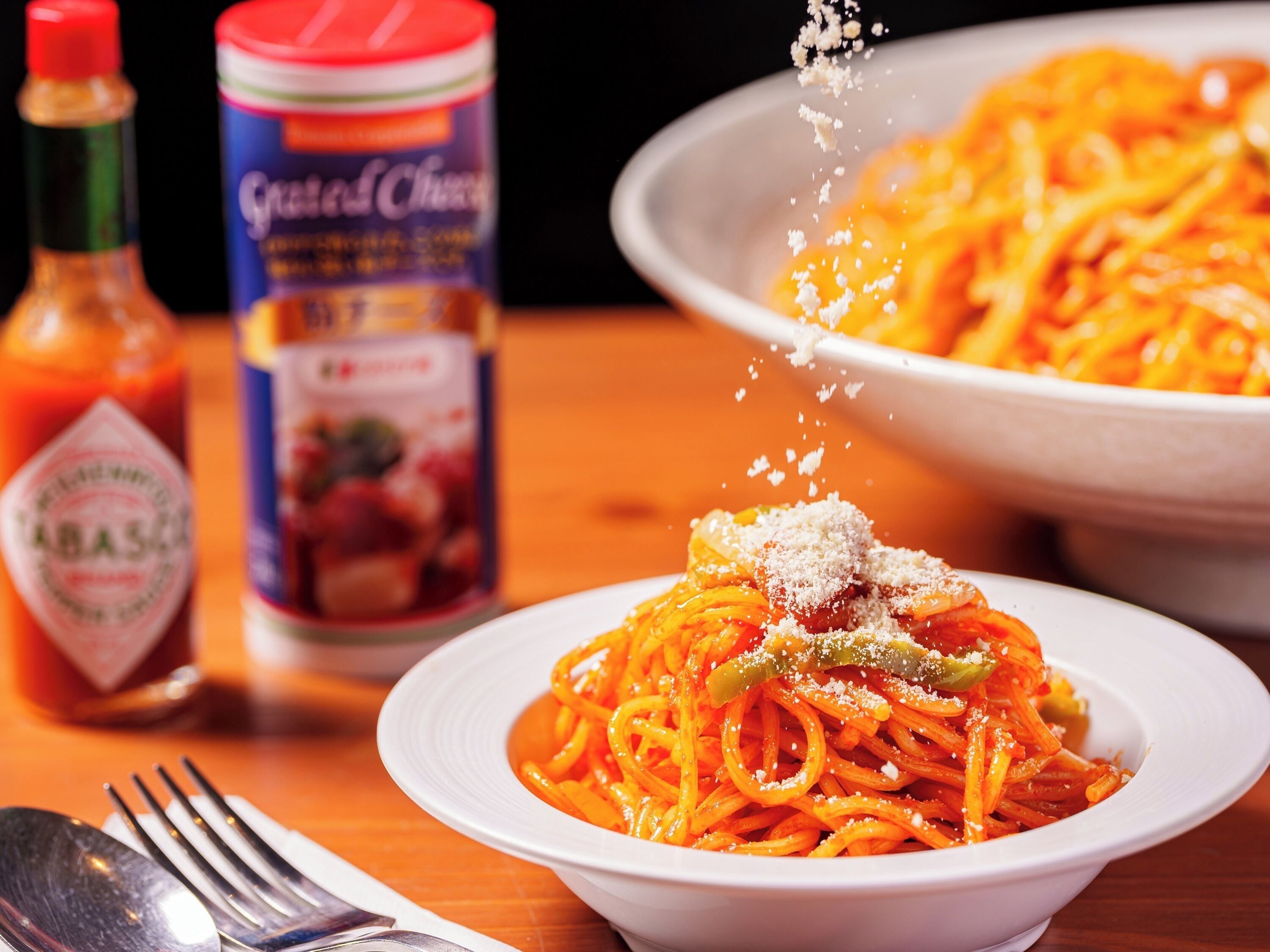 Eine Schüssel Spaghetti, bestreut mit geriebenem Käse und einem Löffel.