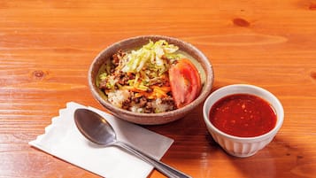 A bowl of food with a side of sauce on a wooden table.