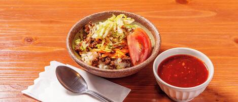 A bowl of food with a side of sauce on a wooden table.