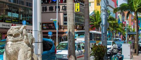 Una calle urbana concurrida con una estatua de león de piedra, coches y un autobús.