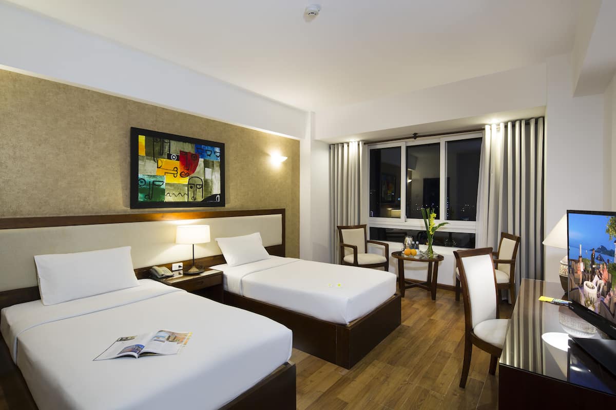 Habitación de hotel con dos camas, un escritorio, un televisor, una silla y un cuadro en la pared.