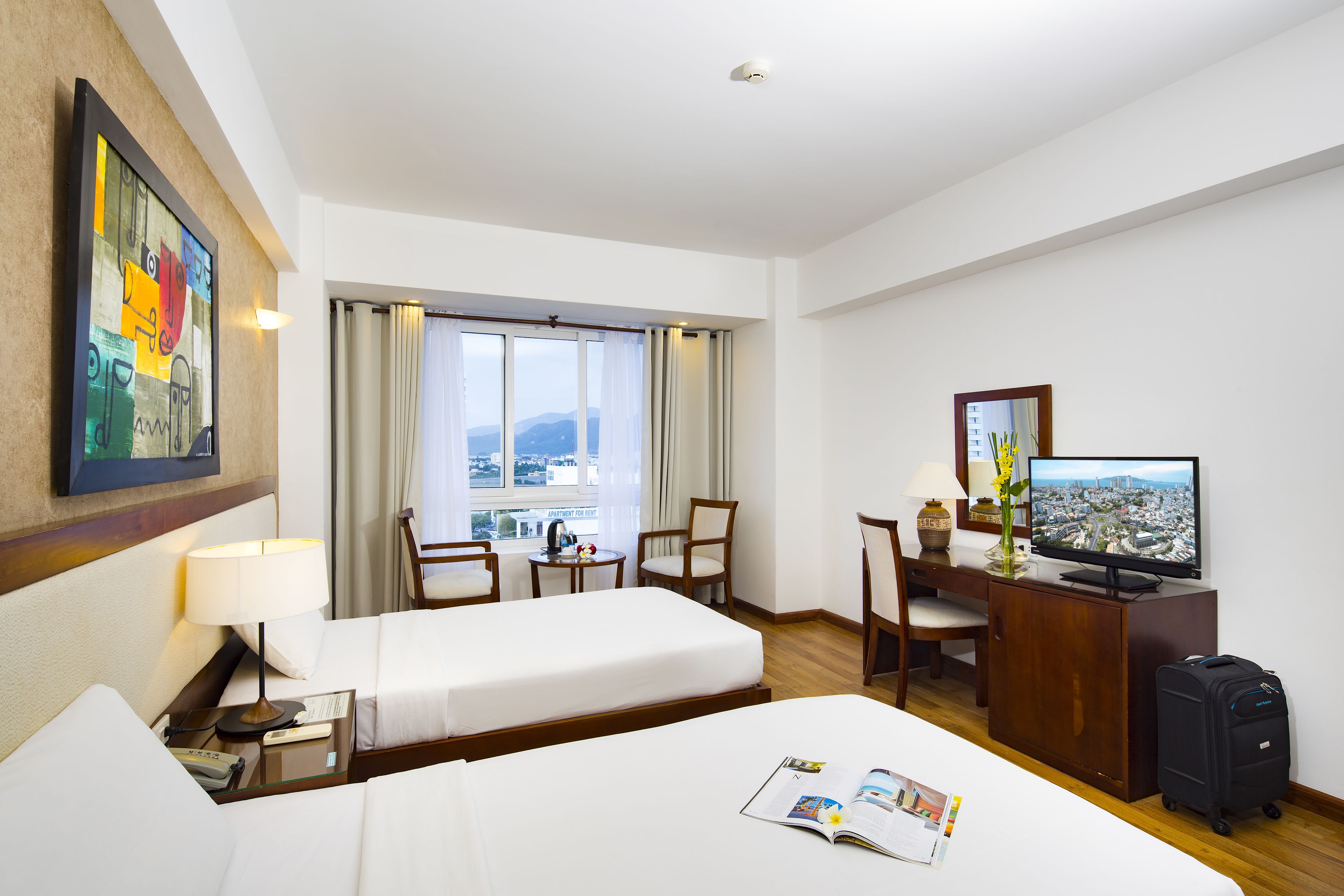 A hotel room with two beds, a desk with a TV, a chair, and a view of the city.
