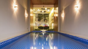 Piscina con baldosas azules formando un diseño de cuadros, rodeada de muros con luces y vistas a un paisaje urbano a través de un muro de cristal.