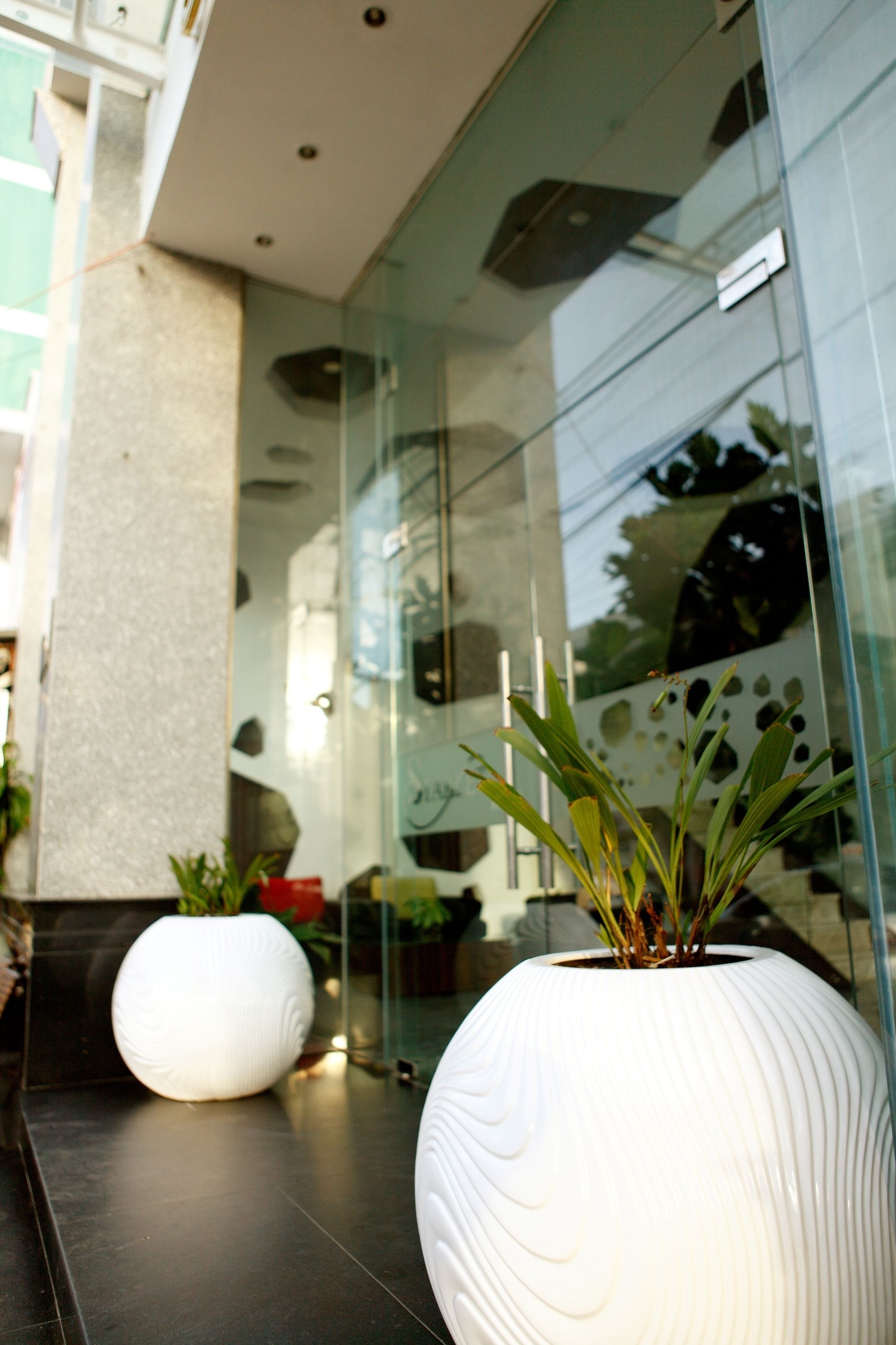 Exterior de un edificio moderno con ventanas de vidrio reflectante y dos grandes macetas blancas con plantas.