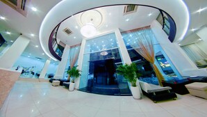 Un hall d’hôtel moderne doté d’un plafond incurvé, d’un comptoir d’accueil, d’espaces aménagés pour s’asseoir et de plantes en pot.
