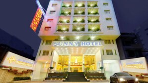 Un hôtel à plusieurs étages, reconnaissable à son grand panneau « Sunny Hotel », à son entrée bien éclairée et à une voiture garée devant.