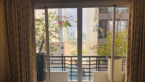 Un balcon avec un lit, une plante en pot et une vue sur des bâtiments et de la verdure.