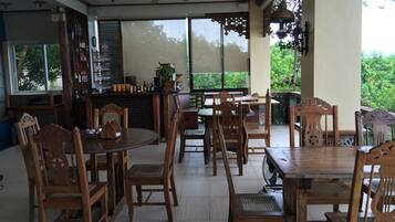 A spacious indoor area with wooden furniture, a bar area, and large windows offering a view of greenery.