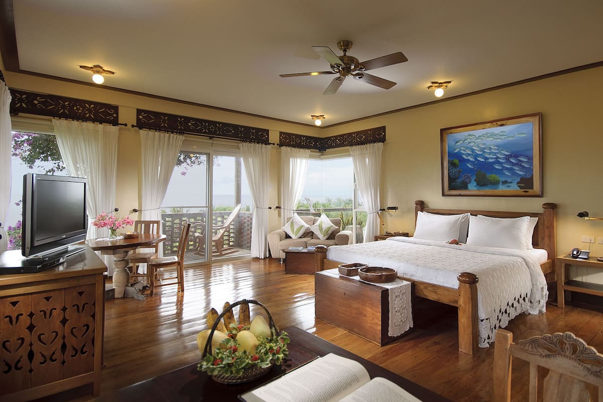 A spacious bedroom with a large bed, a television, and a balcony with a view of the ocean.